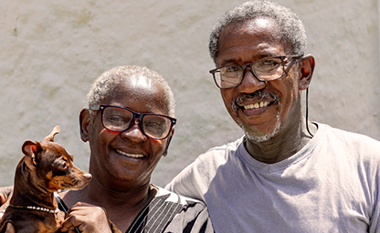 [Imagem de um casal de idosos sorrindo com um cachorro]